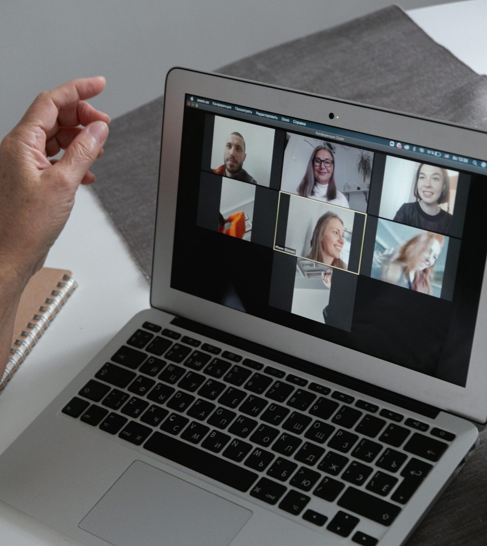 Hands at a laptop showing a group video call in a home office setting.