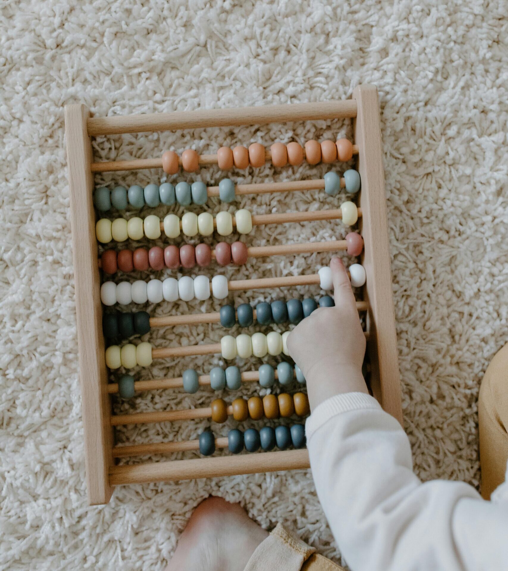 Overhead view of a child using a colorful wooden abacus on a carpet.